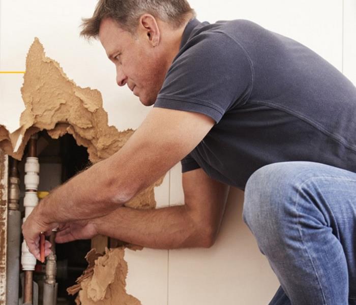 Man with tools with drywall torn out fixing a pipe